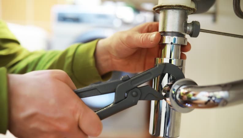 Plumber using pliers to tighten a pipe under a sink