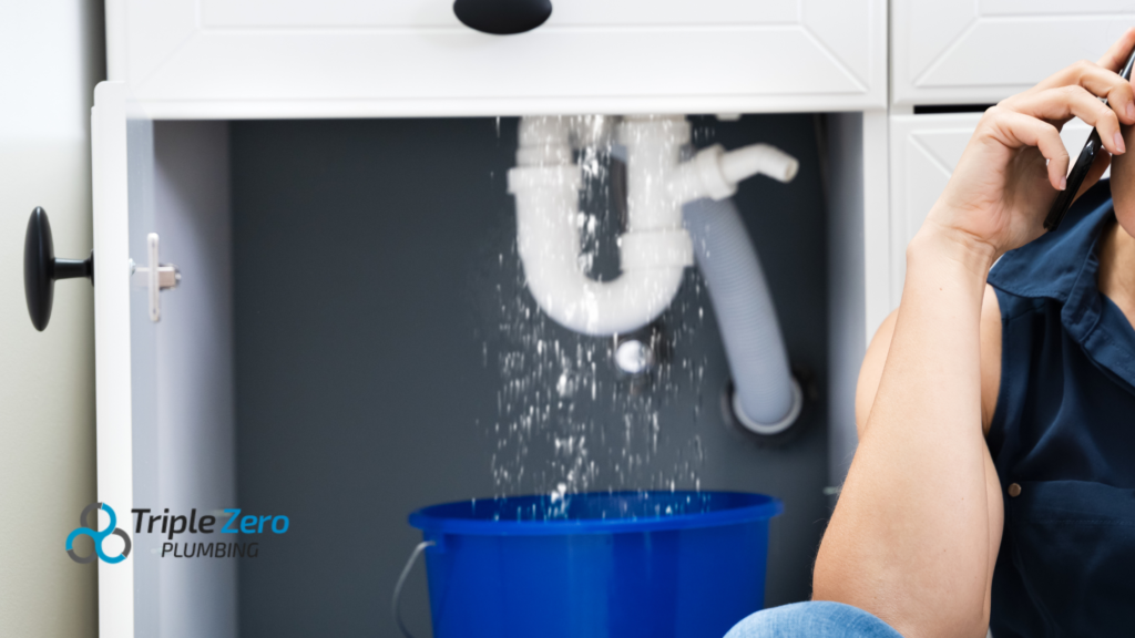 Person calling a plumber while water leaks from a pipe under a sink